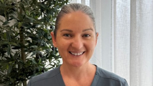 Smiling dental assistant in grey scrubs sharing her honest Invisalign journey experience