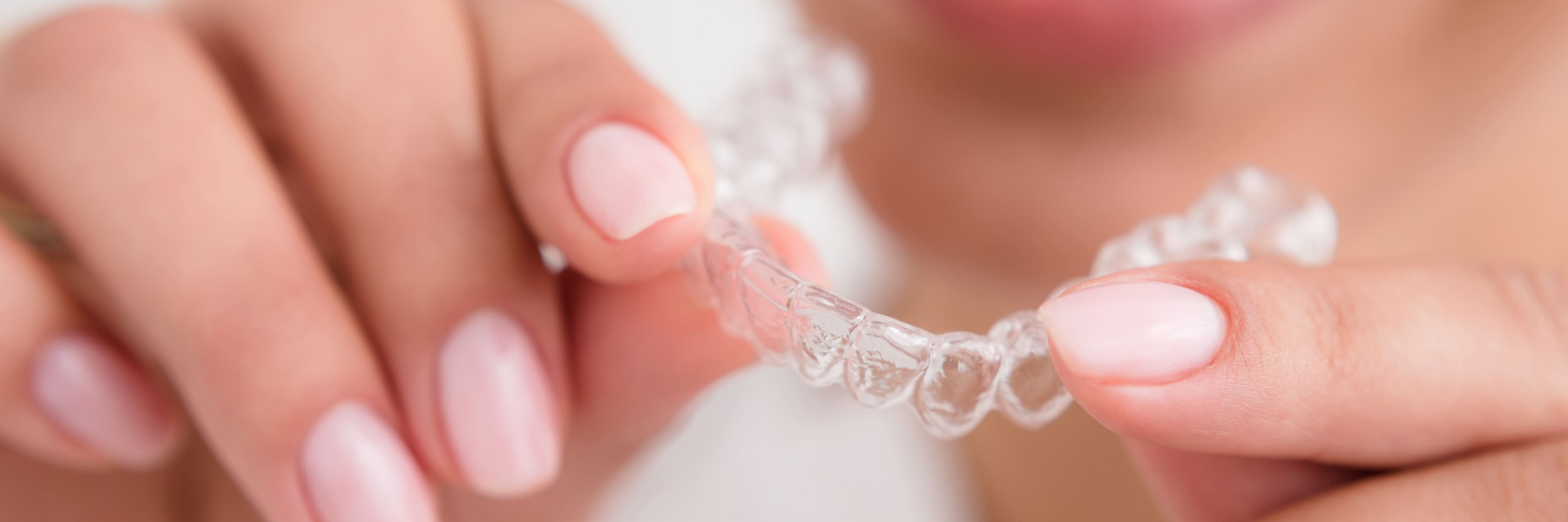 Woman holding a clear Invisalign aligner tray close to her face