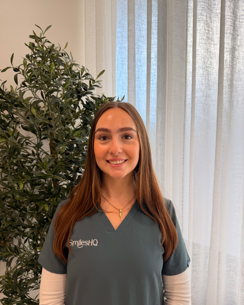 Olivia, dental assistant, smiling warmly in SmilesHQ scrubs in modern dental office setting